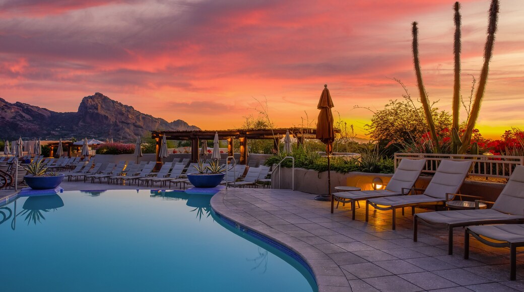 A poolside area with lounge chairs and a view of mountains during sunset.