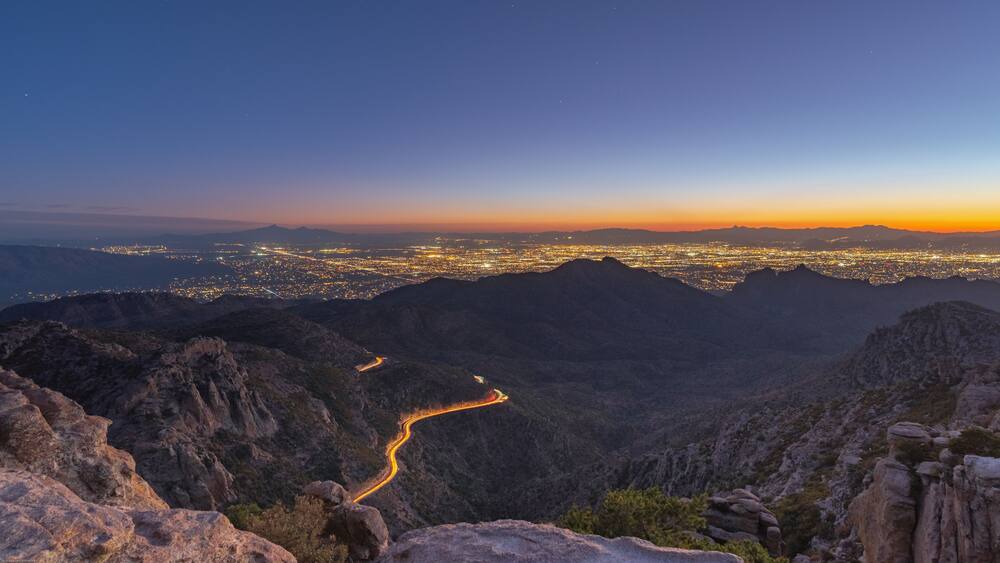 Un paysage montagneux, avec une route sinueuse et une ville illuminée au loin.