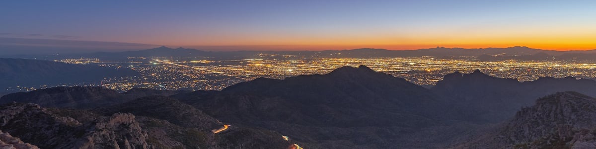 Un paysage montagneux, avec une route sinueuse et une ville illuminée au loin.