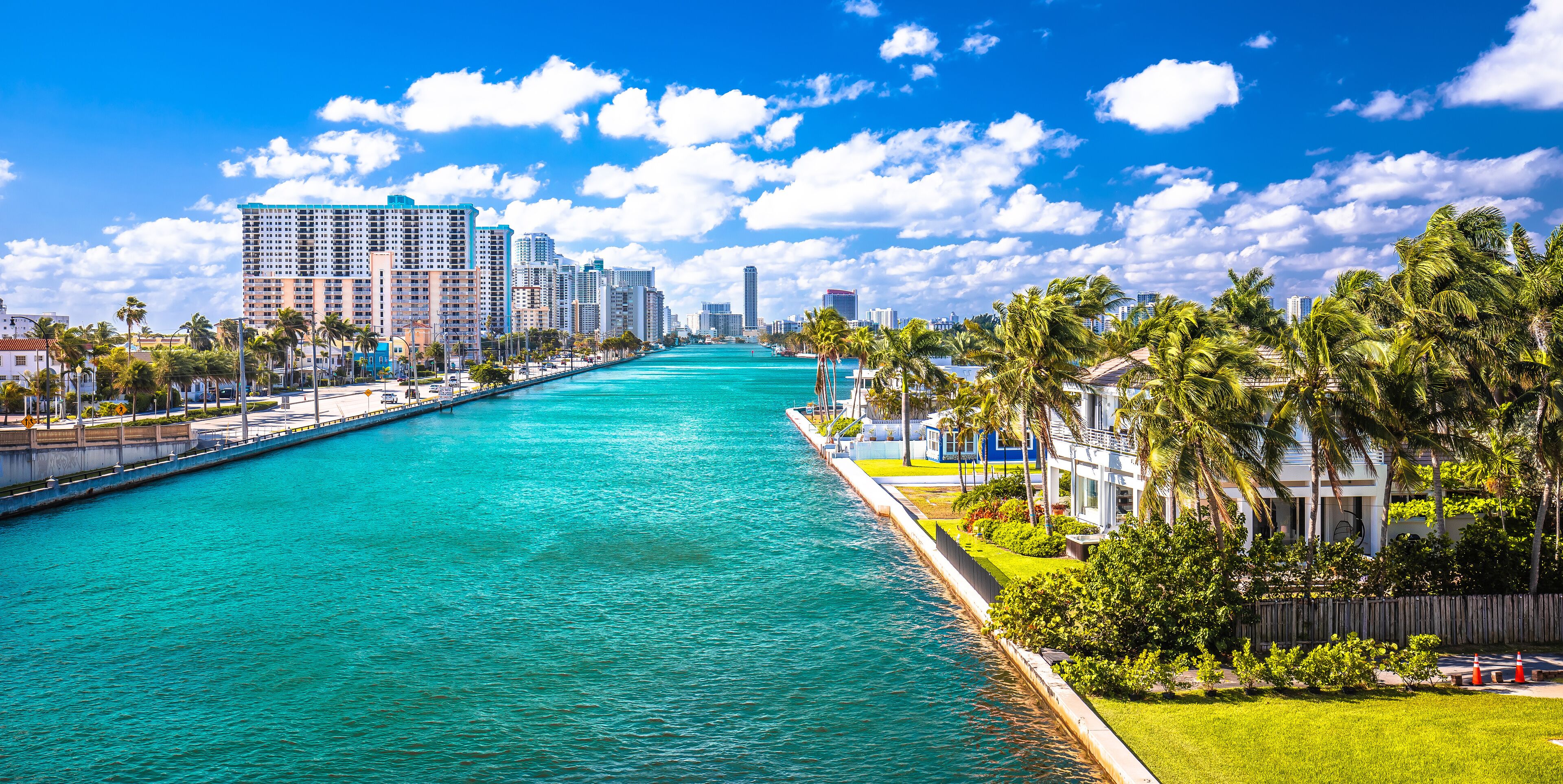 A waterfront cityscape with a turquoise river, tall buildings, and palm trees.