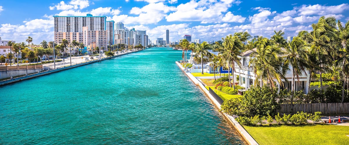 A waterfront cityscape with a turquoise river, tall buildings, and palm trees.
