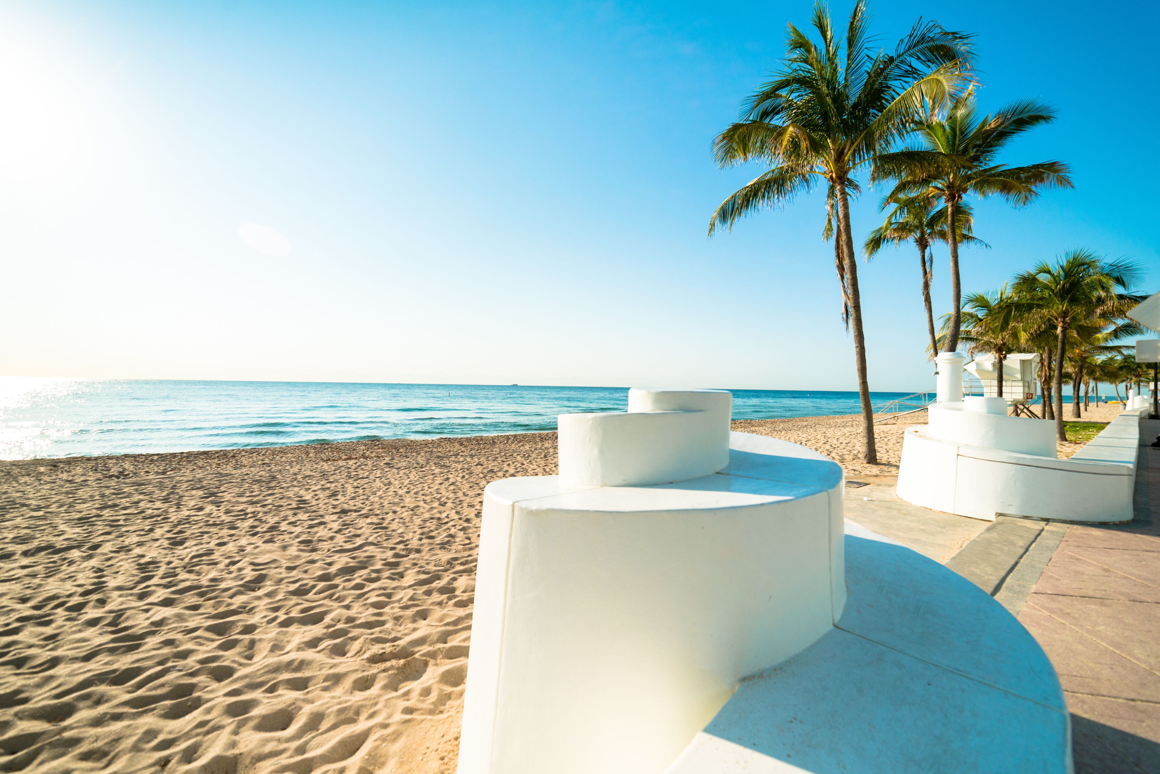 A sandy beach with white planters and palm trees.