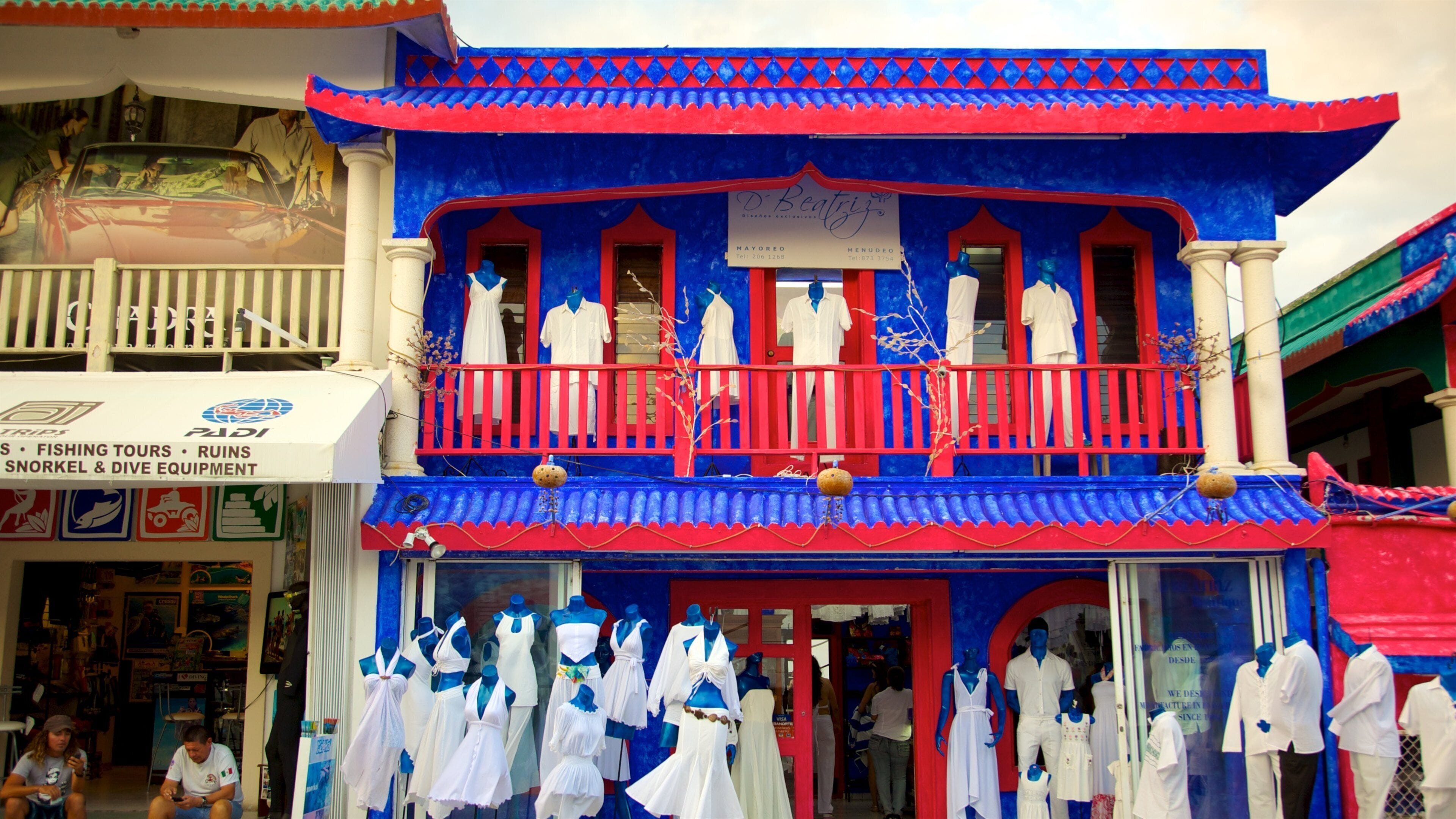 A brightly colored building with blue and red accents, mannequins dressed in white, and a sign advertising fishing tours and dive equipment.