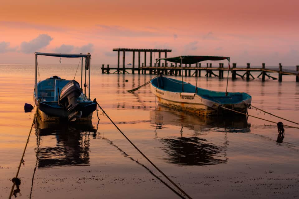 Two boats tied to a dock with a pier in the background during sunset.