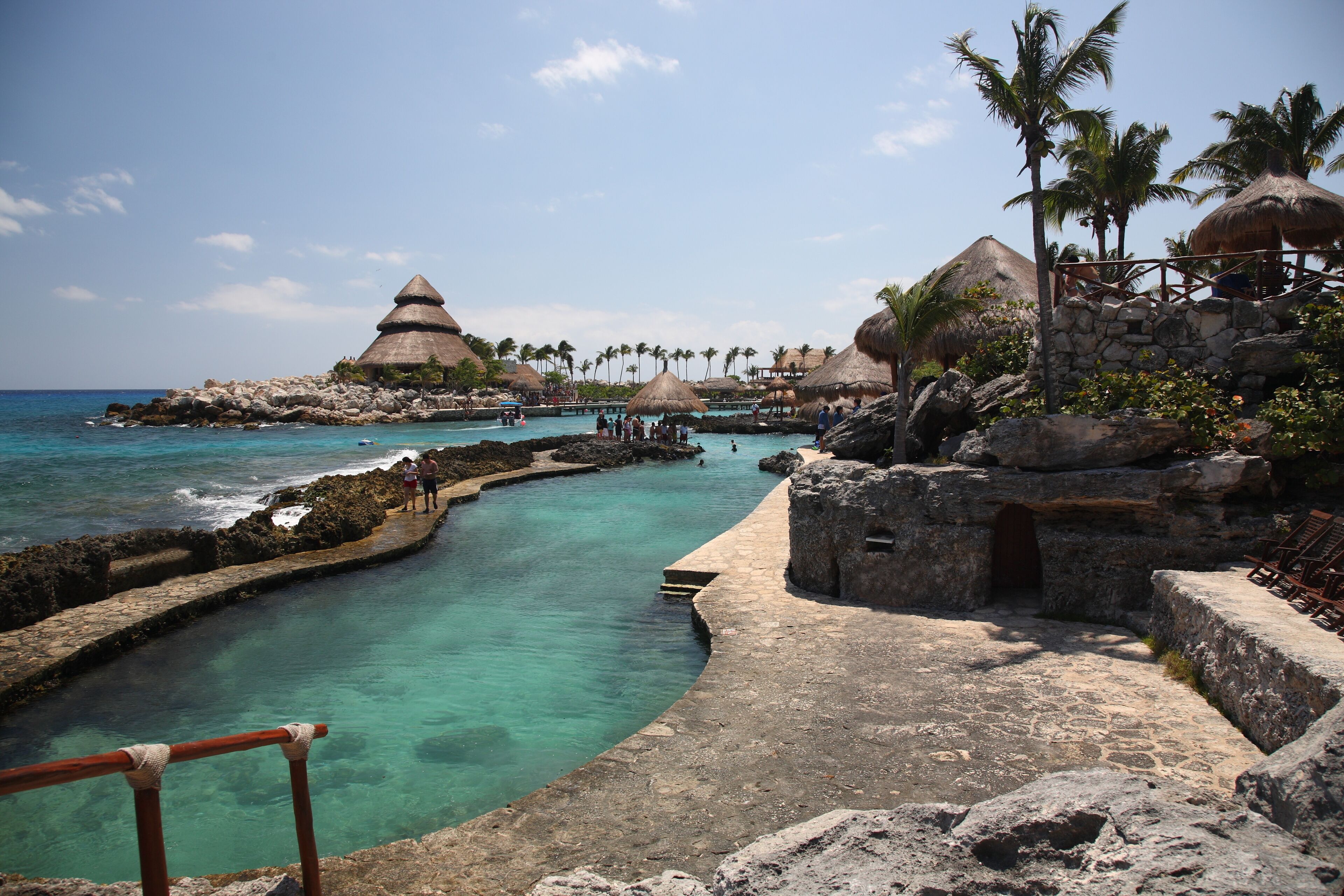 Um resort tropical com águas turquesa cristalinas, estruturas com telhados de palha e palmeiras.