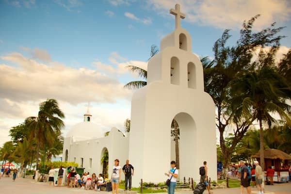 Una iglesia blanca con cruz en la parte superior, rodeada de palmeras y gente.