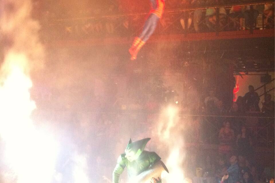 A performer in a green costume suspended above a crowd in a dimly lit venue.