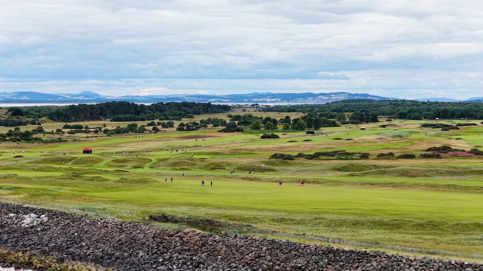 A golf course with rolling hills, a red building, and distant mountains.
