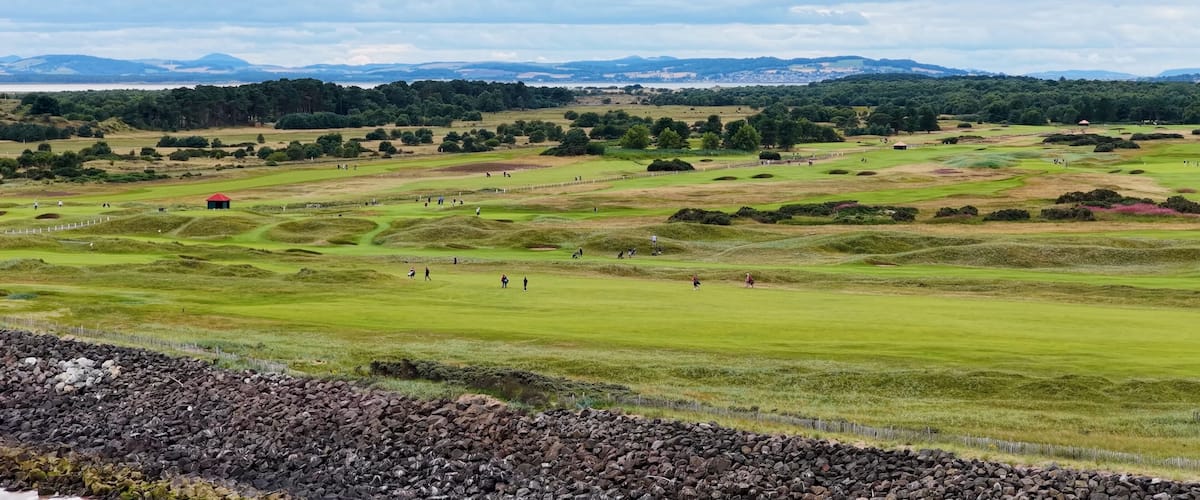 A golf course with rolling hills, a red building, and distant mountains.