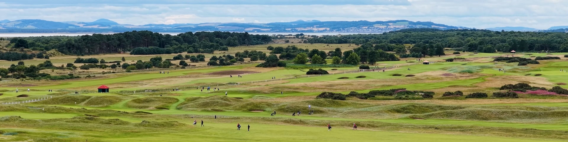 A golf course with rolling hills, a red building, and distant mountains.