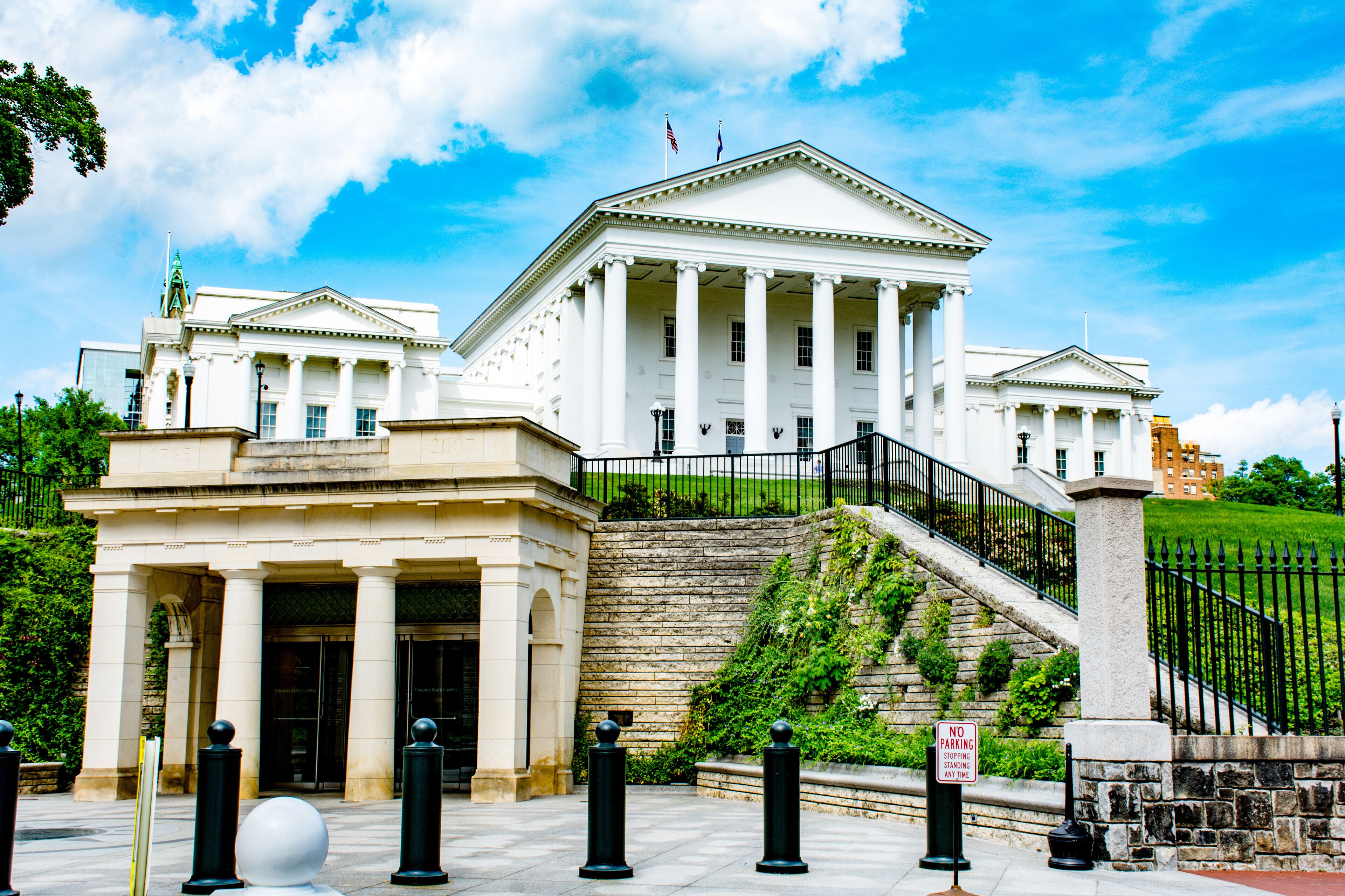 A large white neoclassical building with columns, a flag, and a "No Parking" sign.