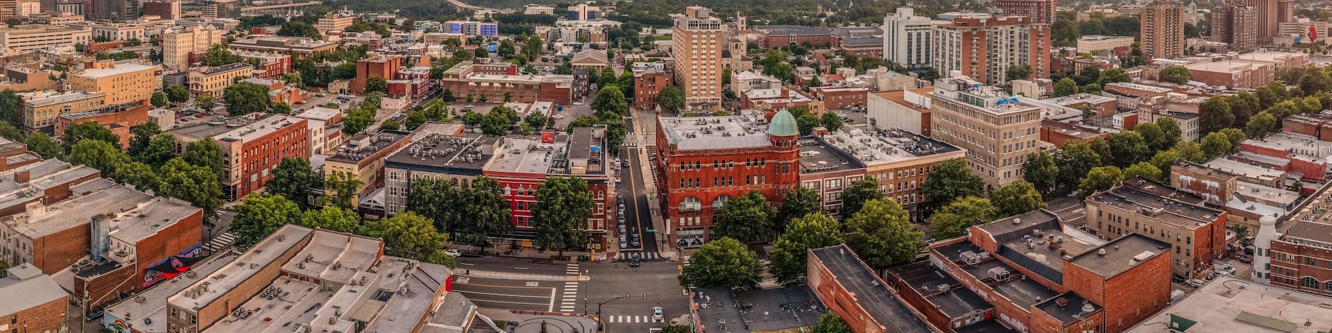 A cityscape with a mix of historic and modern buildings, a prominent red brick building, and a clear sky with scattered clouds.