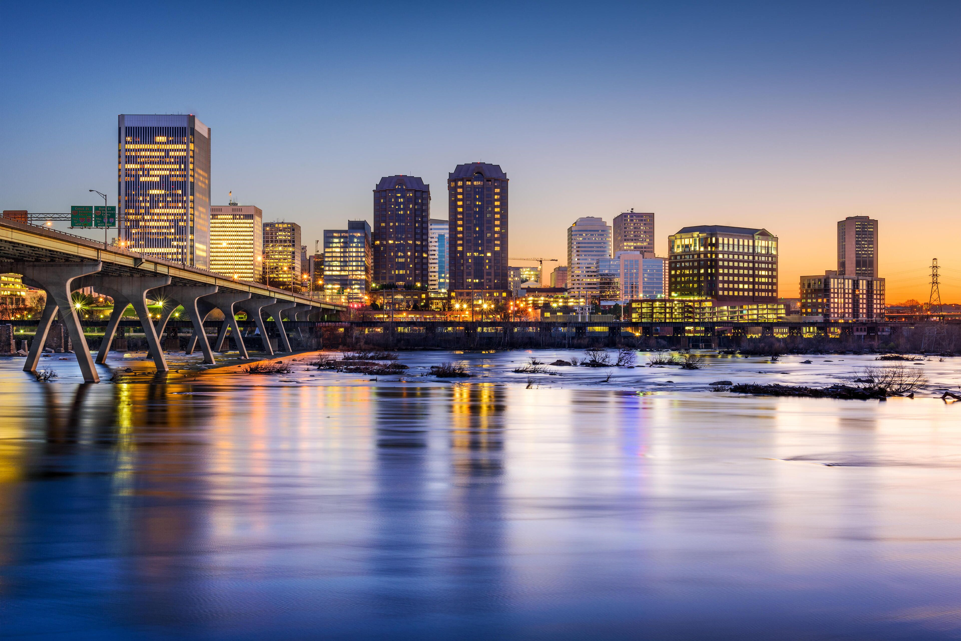 Un horizonte urbano al atardecer con edificios iluminados y un puente sobre un río helado.