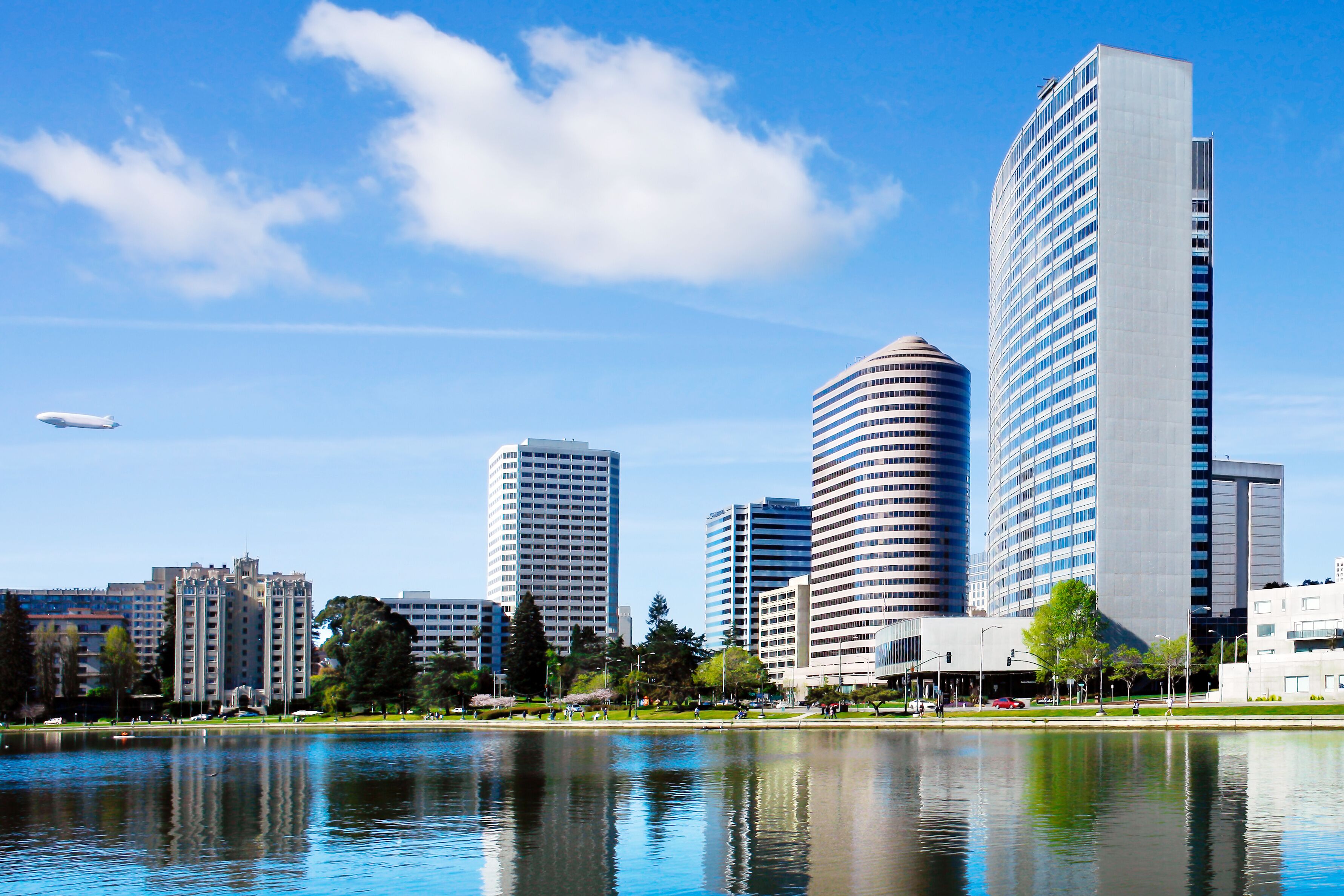 A cityscape with modern high-rise buildings, a body of water reflecting the structures, and a clear blue sky.