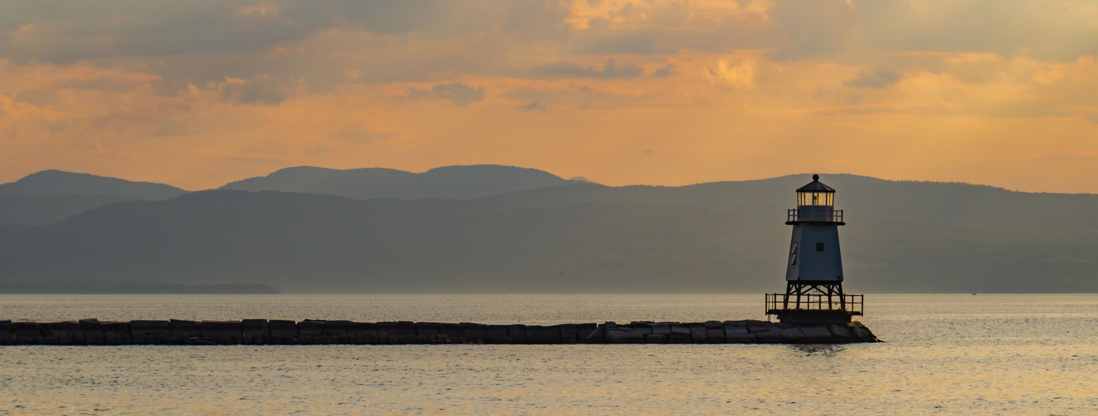 A lighthouse on a rocky outcrop with a mountain range in the background.