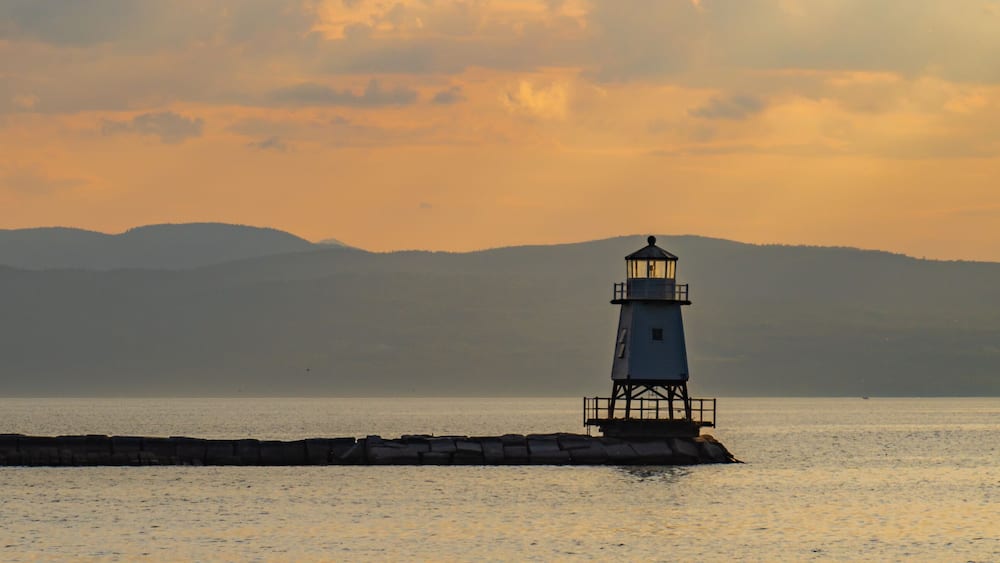 Un phare situé sur un promontoire rocheux, avec une chaîne de montagnes en arrière-plan.