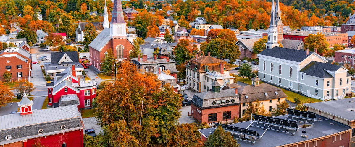 A town with autumn-colored trees, historic buildings, and two prominent church spires.