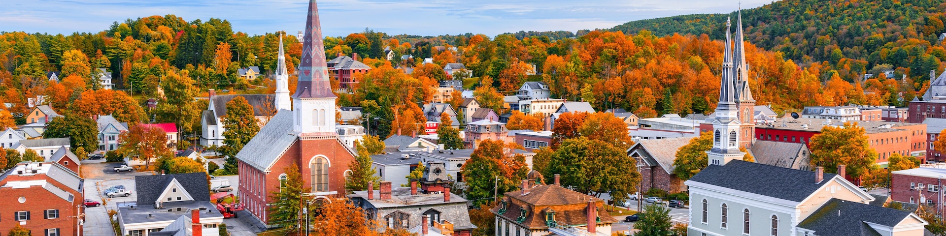 A town with autumn-colored trees, historic buildings, and two prominent church spires.