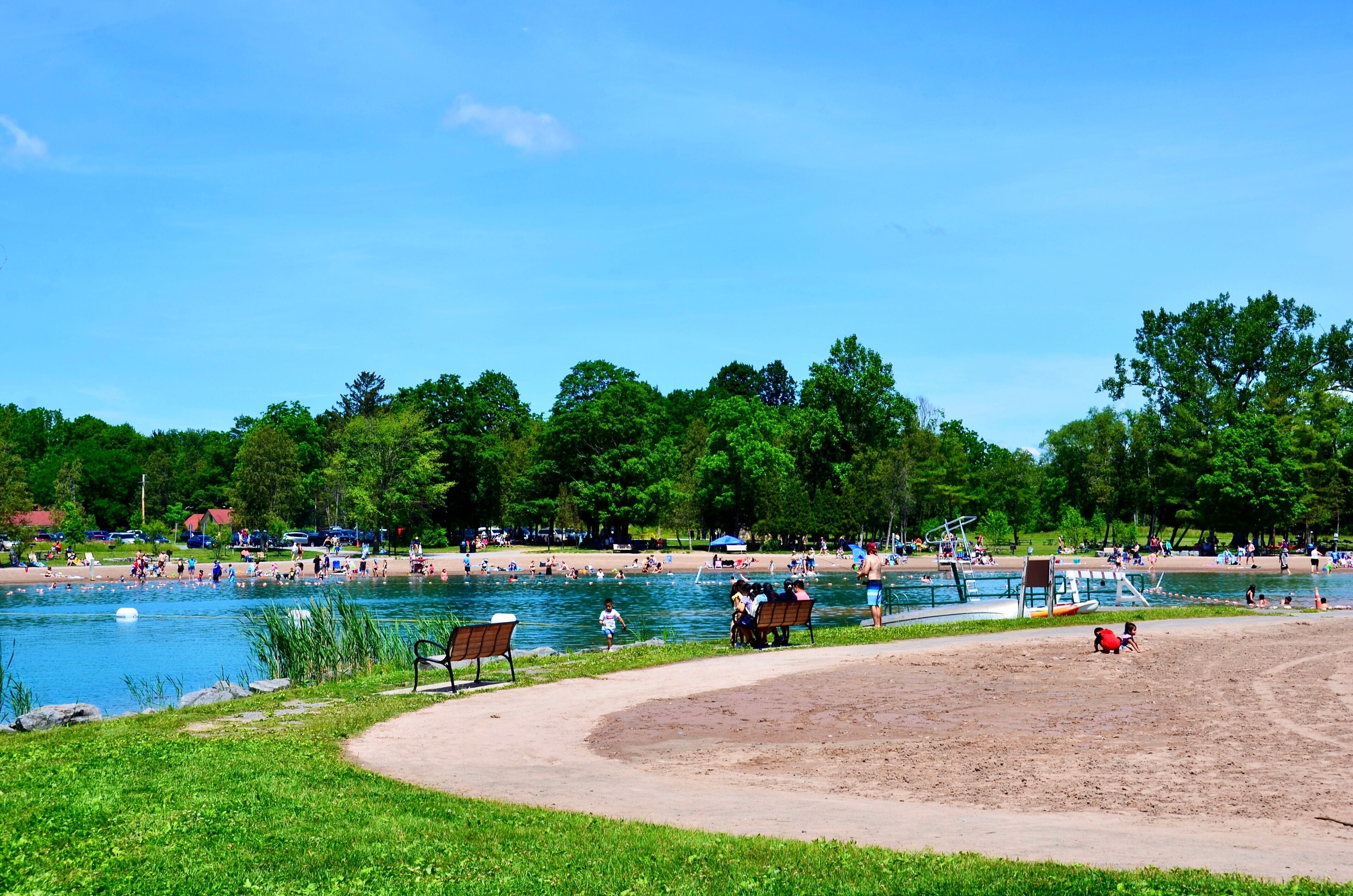 A lakeside park with a sandy beach, a swimming area, and a boat dock.