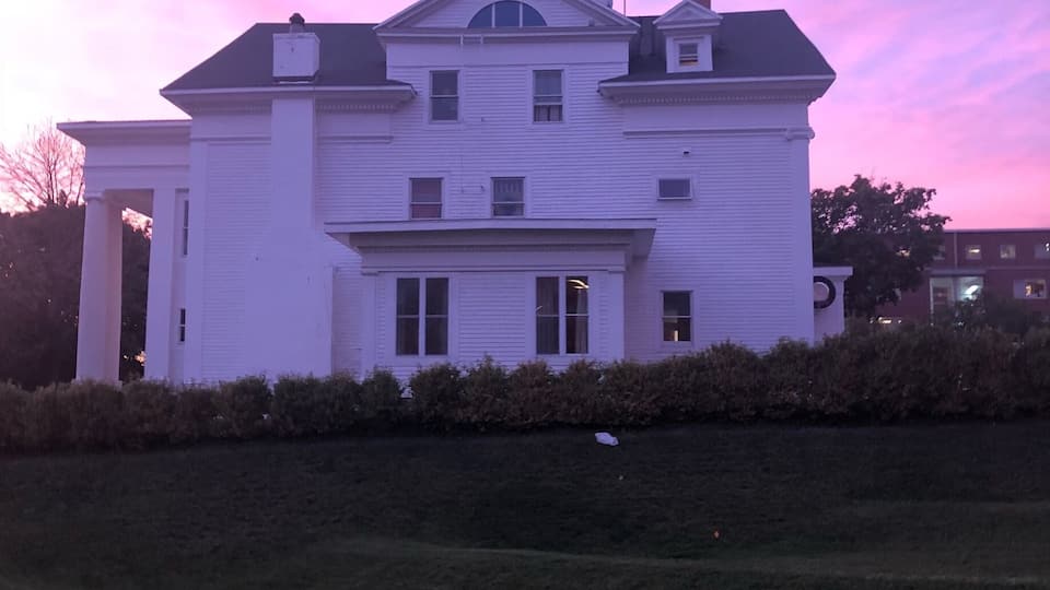A white two-story house with a central entrance and a small tower-like structure on the roof.
