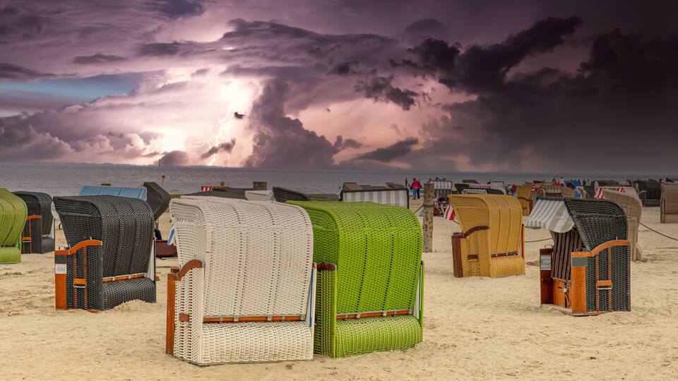 Beach chairs and umbrellas on a sandy beach with a stormy sky.