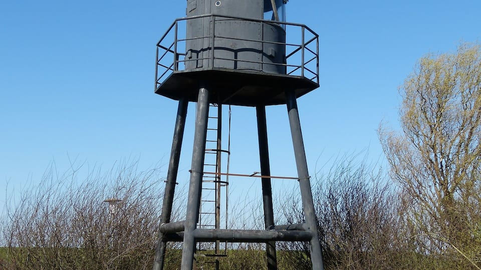 A tall, cylindrical water tower with a rounded top and a metal railing around the base.