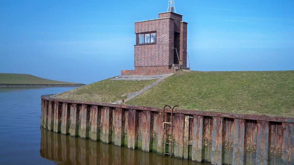 A brick lighthouse on a grassy hill by a calm body of water.
