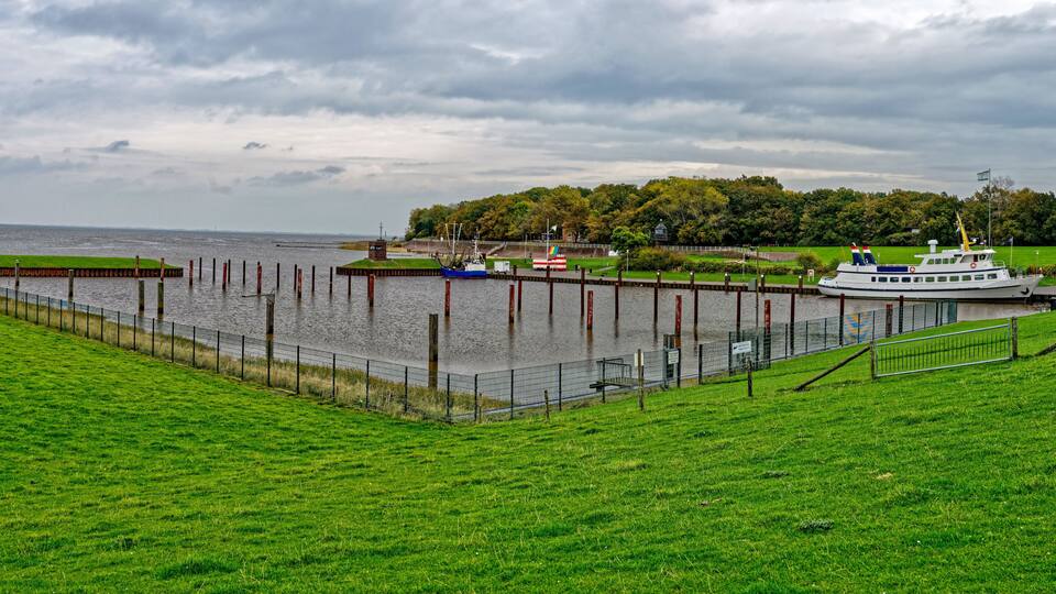 A river with a boat docked at a pier, surrounded by green grass and a cloudy sky.