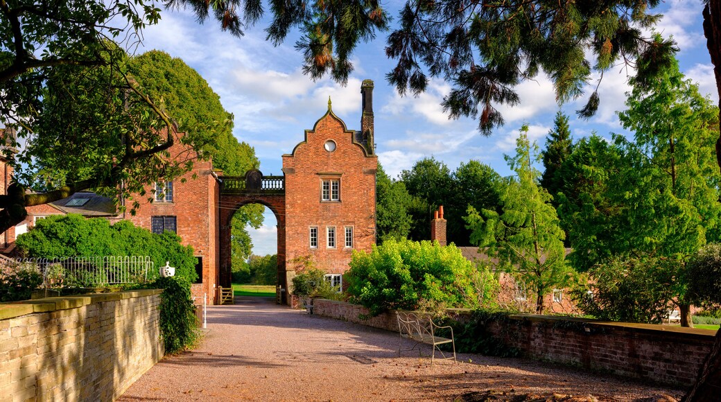 A historic brick building with a prominent archway, surrounded by lush greenery and trees.