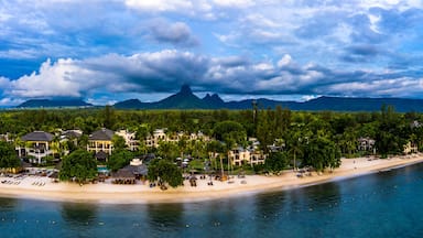 Un complejo turístico frente al mar con villas privadas en la playa, una playa de arena y una montaña al fondo.