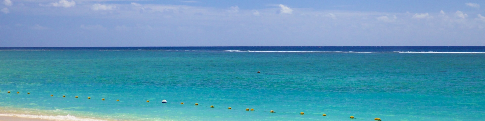 Uma praia com águas turquesa cristalinas, areal arenoso e um pequeno barco inflável com motor e colete salva-vidas.