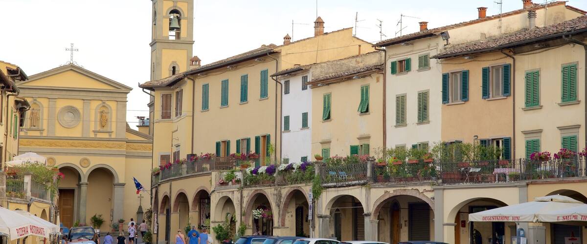 A historic square with a church, a bell tower, and parked cars.