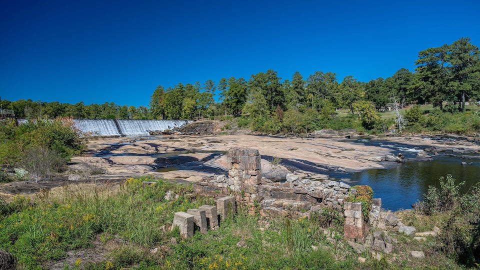 Ancient ruins and a river in a forested area.