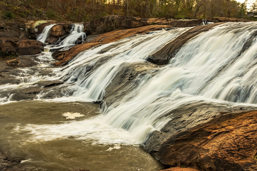 A beautiful landscape photo the waterfalls at High Falls State Park in Georgia as seen through evergreen trees.