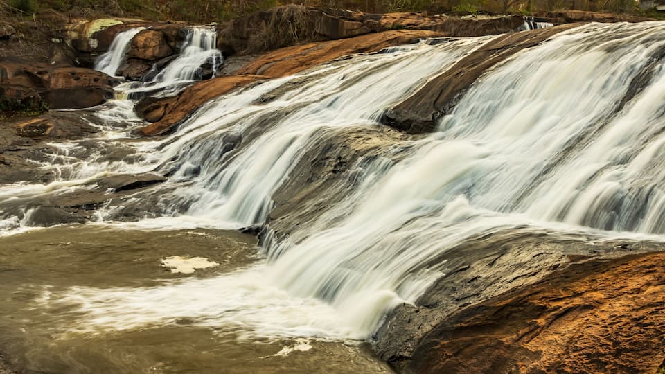 A multi-tiered waterfall cascading over rocky terrain surrounded by trees.