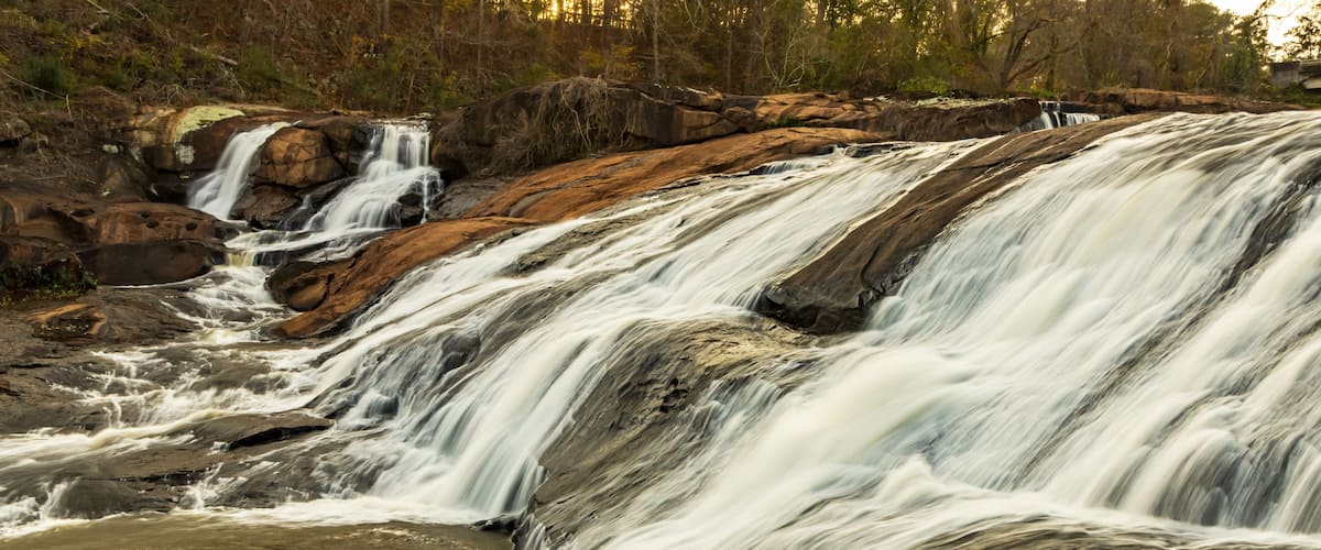 A beautiful landscape photo the waterfalls at High Falls State Park in Georgia as seen through evergreen trees.