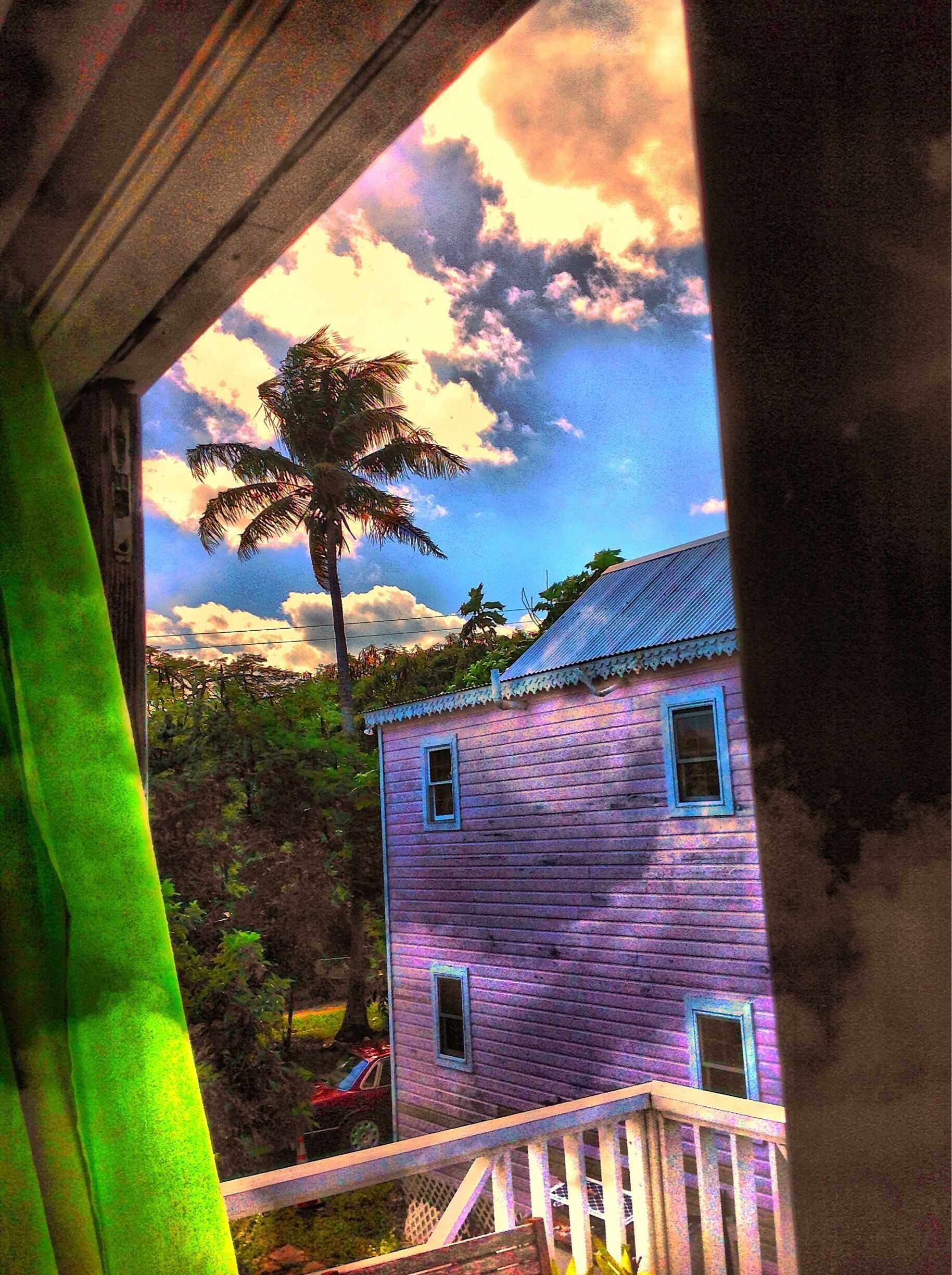 A house with a pink exterior, a palm tree, and a blue sky with clouds.
