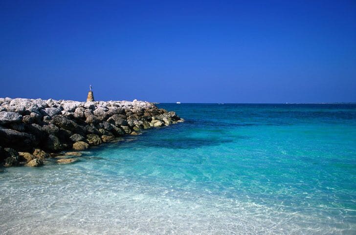 A rocky shoreline with clear turquoise water and a small statue on the rocks.