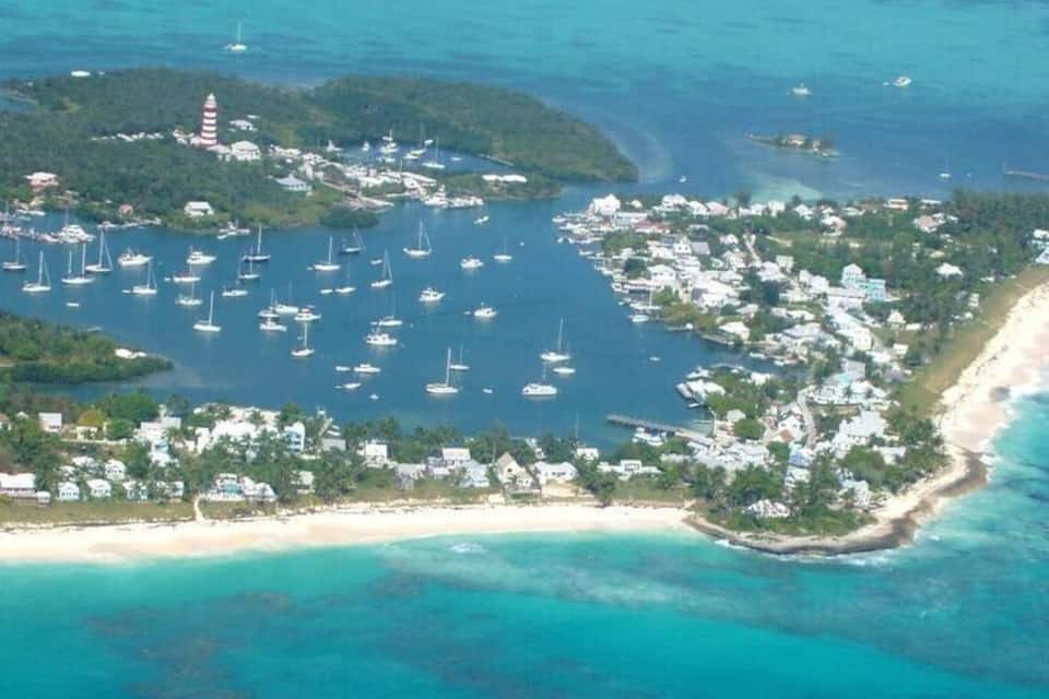 Vue aérienne d’une zone côtière comprenant un port de plaisance, des bateaux, un phare et une plage.