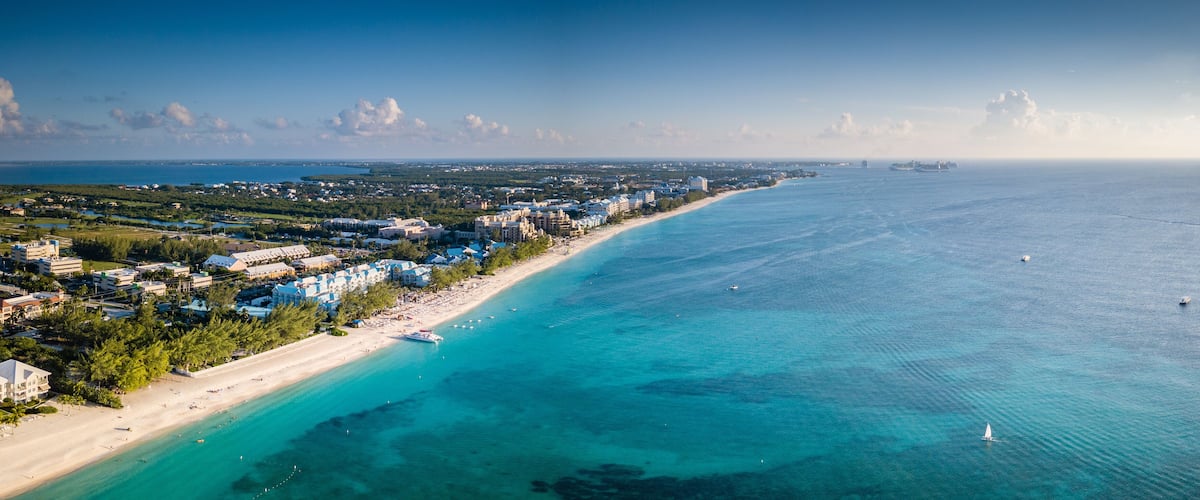 A coastal city with a beach, clear blue waters, and a distant ship.