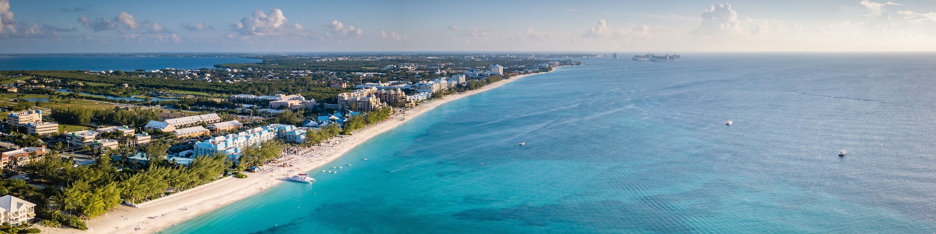 A coastal city with a beach, clear blue waters, and a distant ship.