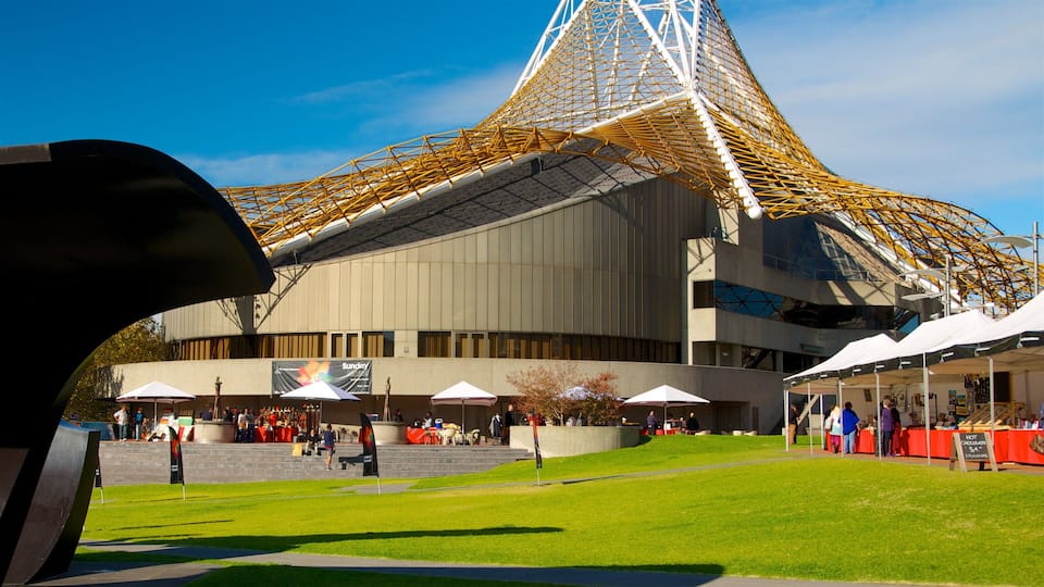 A modern building with a distinctive golden lattice roof, surrounded by green grass and outdoor seating areas.
