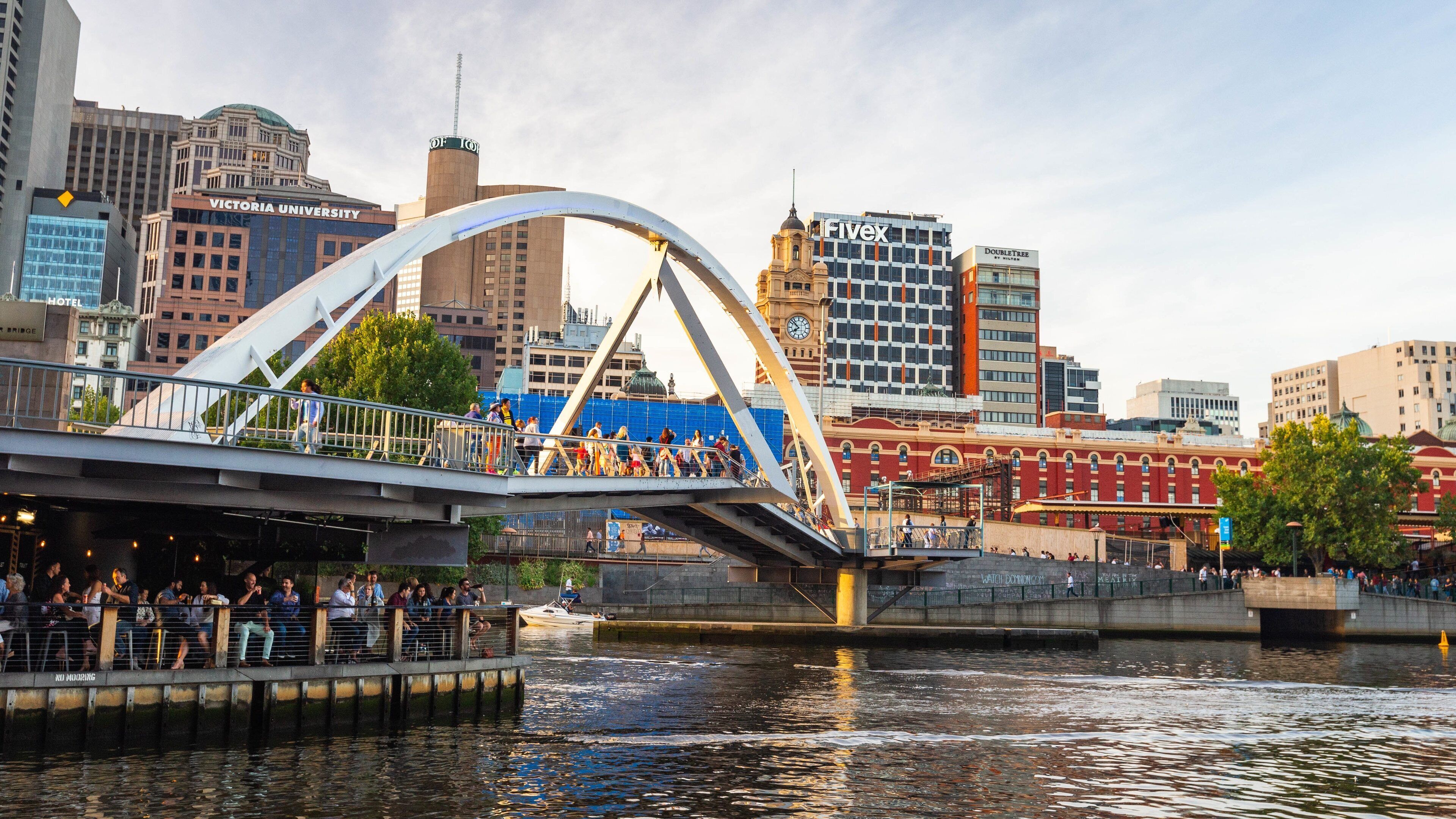 Un puente con gente caminando, un río y edificios al fondo.