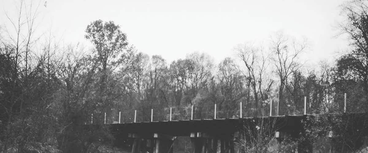 A gravel road under a wooden bridge surrounded by trees.