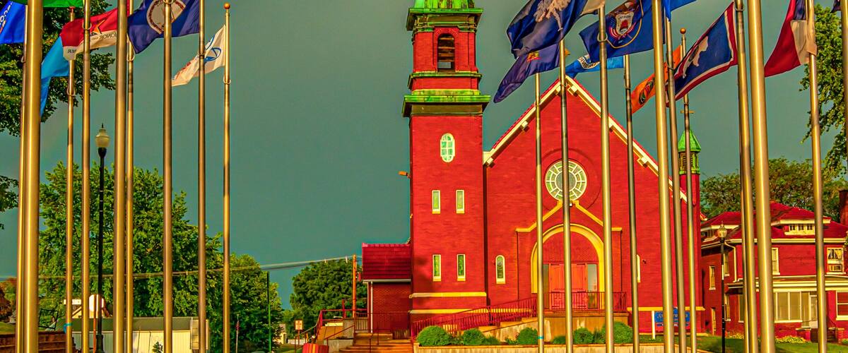 A red church with a green spire, surrounded by flags, under a rainbow.