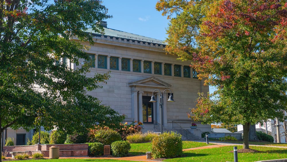 A classical building with a green roof, surrounded by well-maintained lawns and trees with autumn foliage.