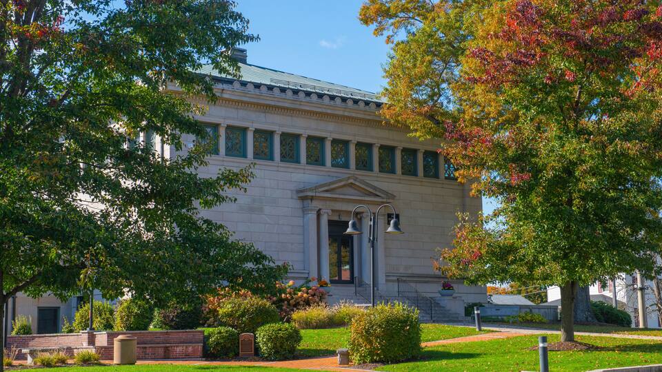 A classical building with a green roof, surrounded by well-maintained lawns and trees with autumn foliage.
