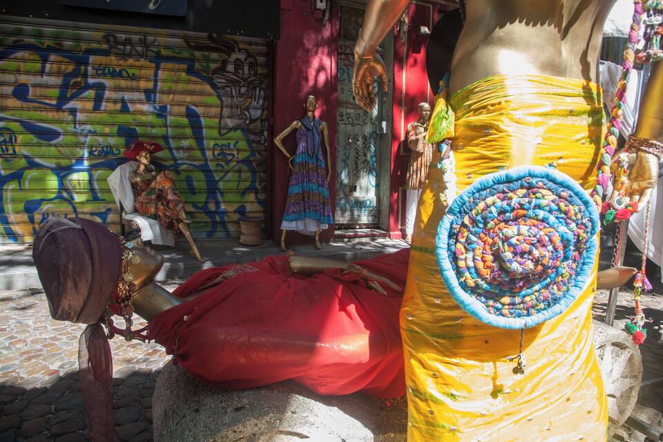 A street scene with a mannequin in a yellow dress, a red cloth, and a graffiti-covered wall.
