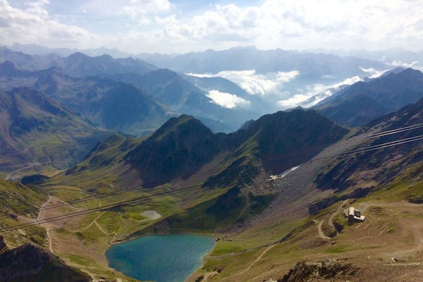 Un paysage montagneux avec un lac, un pont et des montagnes à l’horizon.