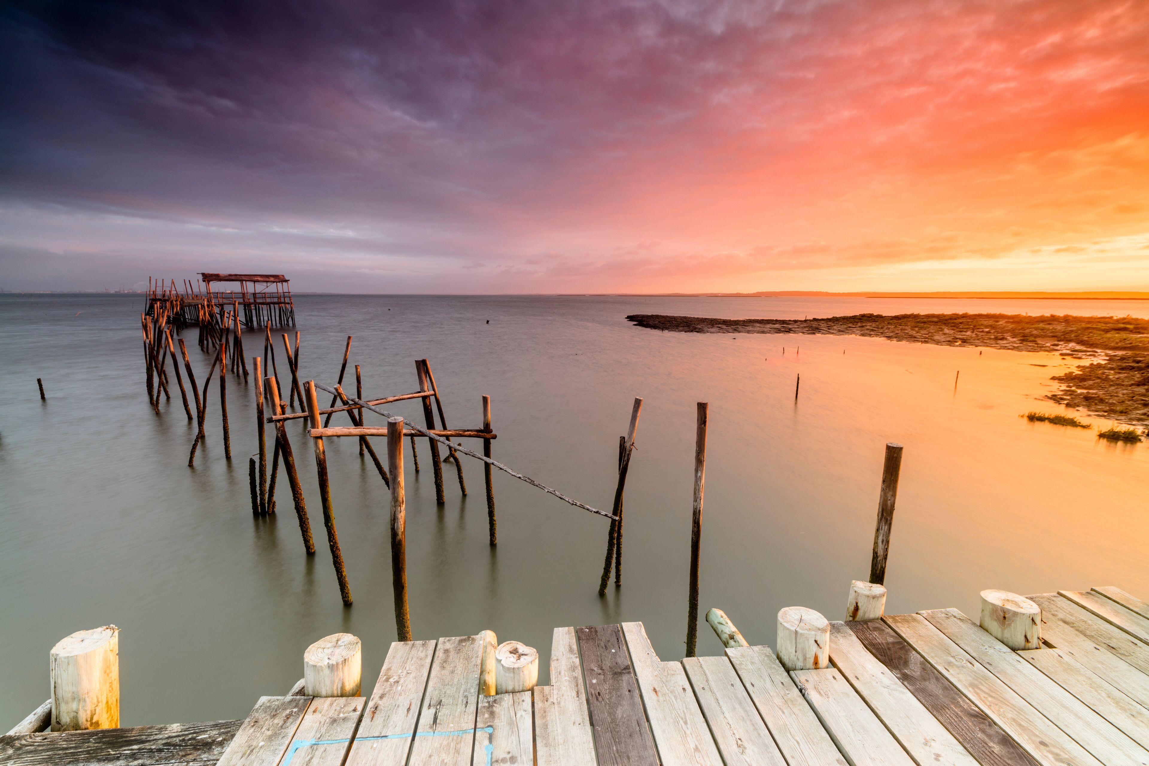 A wooden pier extending into calm waters at sunset.